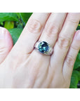 Men's 14K white gold ring with a deep greenish-blue oval sapphire and diamond accents on a hand.