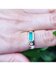 Ring with a genuine colombian emerald on a finger against a green leaf background.