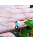 A person's hand wearing a mens emerald ring in yellow gold on a leafy background.