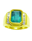 A bezel set natural emerald ring for men with accent diamonds crafted in 18k yellow gold.