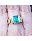 This yellow gold men's emerald ring is in bezel set and has accent natural diamonds on a person's finger.