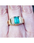This 18k yellow gold men's emerald ring is in bezel set and has accent natural diamonds on a person's finger.