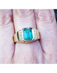 This 18k yellow gold men's emerald ring is in bezel set and has accent natural diamonds on a person's finger.