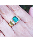 An emeral-cut men's emerald ring in yellow gold with natural accent diamonds on a person's finger.