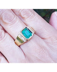 An emeral-cut men's emerald ring in yellow gold with natural accent diamonds on a person's finger.
