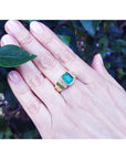 A close view of a hand wearing a natural colombian emerald ring for men against a leafy background.
