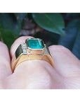 Gold ring for men with accent natural diamond on a finger against a leafy background.