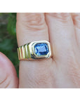 Gold ring with a blue natural blue sapphire gemstone on a hand against a blurred green background