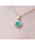Colombian round cut emerald and diamond pendant on a 14K yellow gold minimalist necklace.