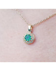 Colombian round cut emerald and diamond pendant on a 14K yellow gold minimalist necklace.