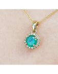 Round cut 0.61 ct. deep green Colombian emerald necklace with halo diamonds in 14k yellow gold.