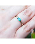 A 14k yellow gold minimalist natural emerald solitaire ring on a person's finger.