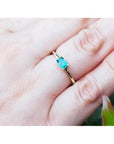 A 14k yellow gold minimalist natural emerald solitaire ring on a person's finger.