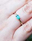 A yellow gold minimalist emerald ring on a person's finger