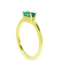 A yellow gold minimalist solitaire emerald ring in its side position.
