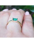 A yellow gold emerald ring on a hand against a blurred natural background