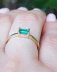 A yellow gold emerald ring on a hand against a blurred natural background