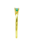 The side position of a minimalist solitaire emerald ring in yellow gold.