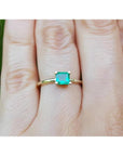 A minimalist emerald solitaire ring in 14k gold representing May's birthstone jewelry on a hand.