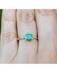 Tis minimalist emerald solitaire ring representing May's birthstone jewelry on a hand against a natural background