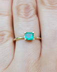 Tis minimalist emerald solitaire ring representing May's birthstone jewelry on a hand against a natural background