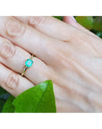 Emerald gold ring on a hand with a green leaf background.