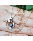 14K yellow gold mother and child pendant necklace with an oval blue sapphire, held by a hand.