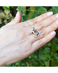 Hand displaying a yellow gold necklace with a mother and child pendant against a green leafy background