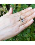 14K yellow gold mother and child sapphire slider pendant necklace held in a hand.