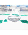 White gold bangle bracelet with diamonds, surrounded by loose green Colombian emeralds and small bags.