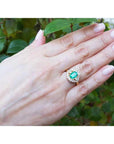 Hand wearing an emerald ring with a green leafy background.