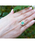 1.43 ct cushion-cut Muzo Colombian emerald ring with marquise diamond halo in 14K yellow gold on a hand.