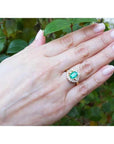 1.43 ct cushion-cut Muzo Colombian emerald ring with marquise diamond halo in 14K yellow gold on a hand.