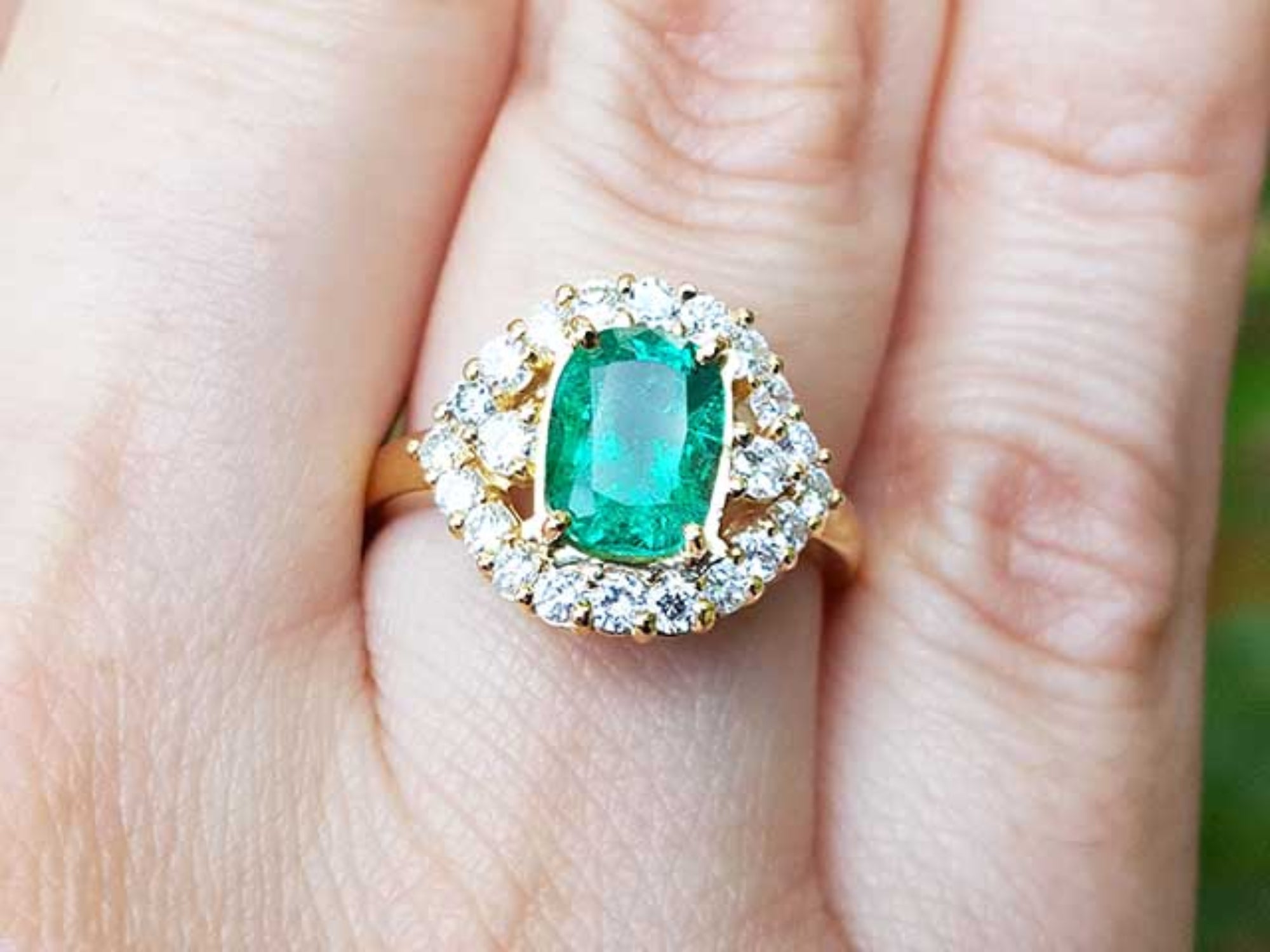 A cushion cut natural Muzo emerald ring with a halo diamond on a finger.