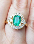 A cushion cut natural Muzo emerald ring with a halo diamond on a finger.