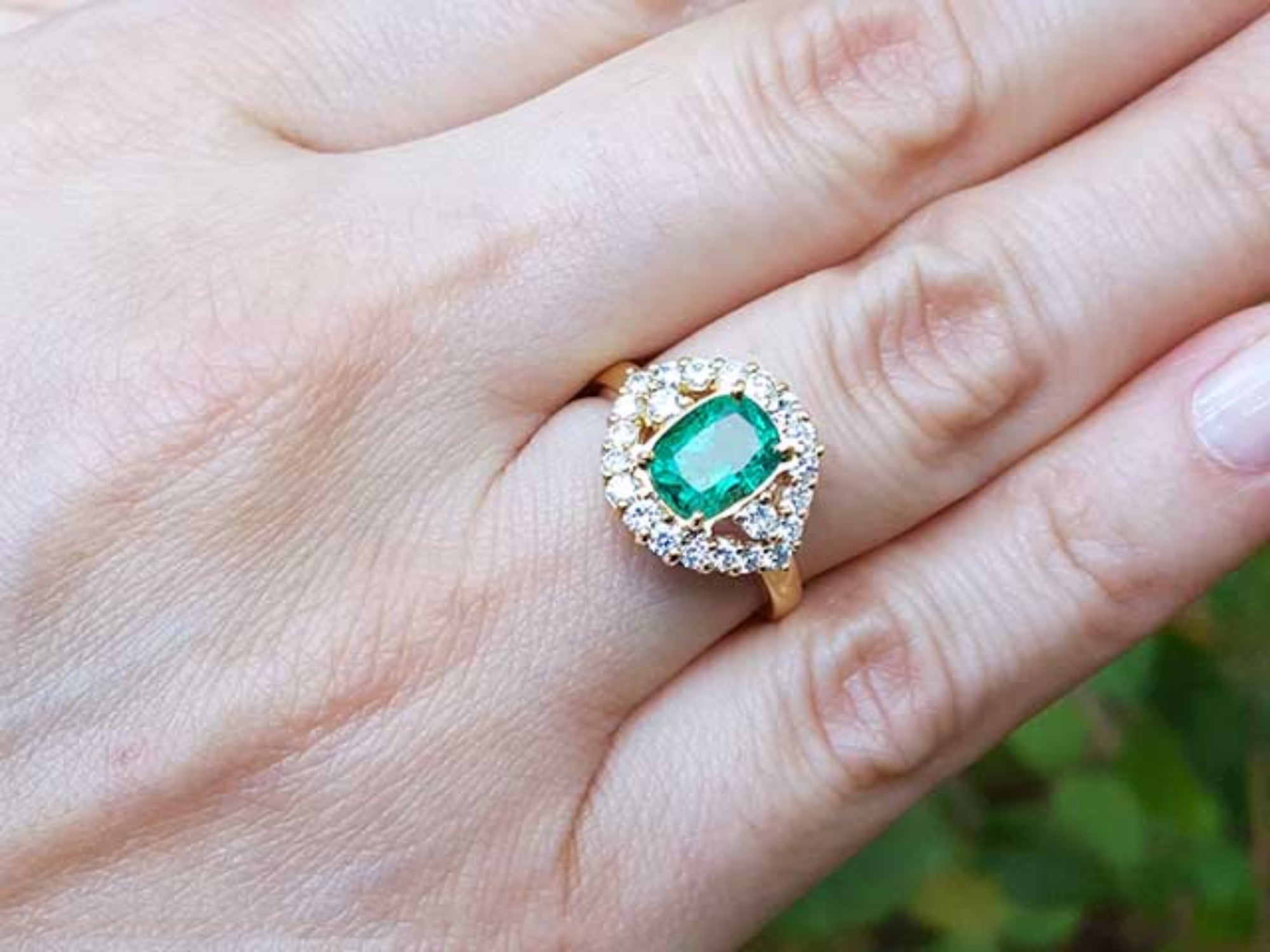 Gold ring with a cushion cut emerald with halo diamond on a hand.