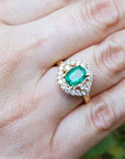 Gold ring with a cushion cut emerald with halo diamond on a hand.