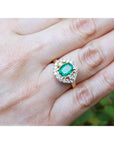 Gold ring with a cushion cut emerald with halo diamond on a hand.