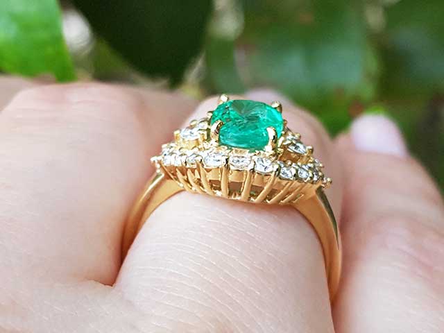 A Muzo born colombian emerald ring in yellow gold on a person's hand.