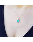 An emerald-cut emerald in a halo diamond pendant on a woman's chest against a natural background.
