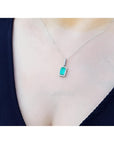 Muzo Colombian emerald pendant with diamond halo on an 18K white gold chain, worn on a person.