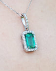 A natural emerald pendant on a silver white gold chain against a beige skin background