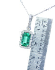 Emerald pendant on a chain with a ruler for scale on a white background