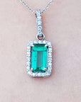White gold emerald pendant with diamond accents on a light pink skin background.