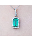 White gold emerald pendant with diamond accents on a light pink skin background.