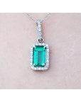 White gold emerald pendant with diamond accents on a light pink skin background.