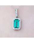 White gold emerald pendant with diamond accents on a light pink skin background.