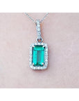 White gold emerald pendant with diamond accents on a light pink skin background.