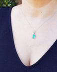 A woman wearing a natural Muzo colombian emerald pendant against a green leafy background.