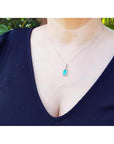 Woman wearing a 1.70 ct. Muzo Colombian emerald pendant with a diamond halo in 18K white gold.